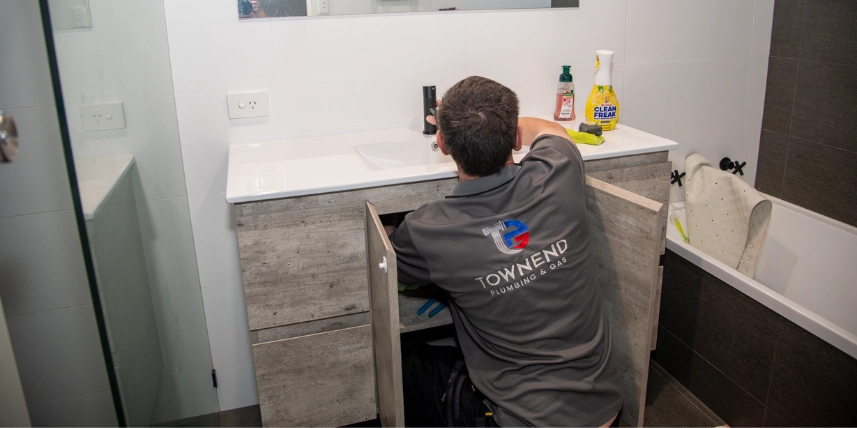 Ashley Townend installing a tap under a bathroom vanity